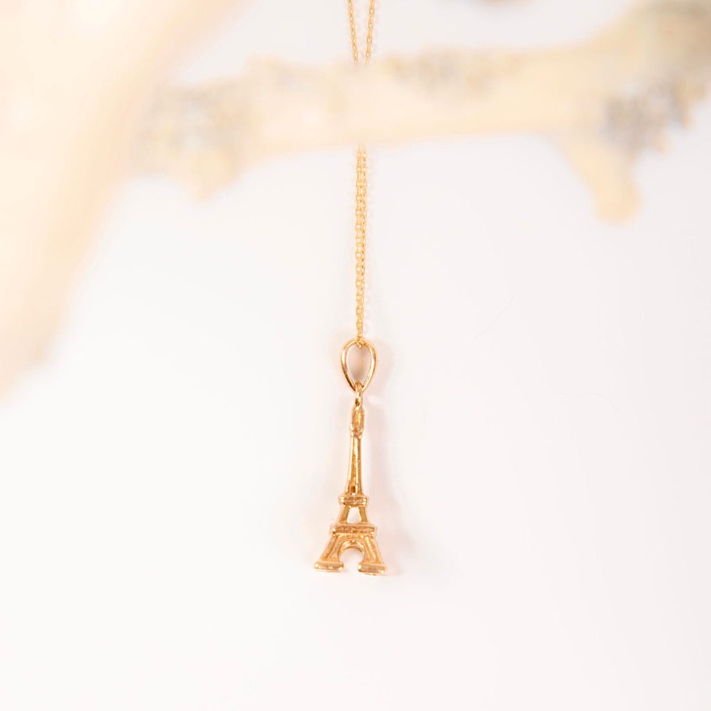 A 14K yellow gold Eiffel Tower pendant displayed against a plain background, highlighting its intricate detailing and polished finish.