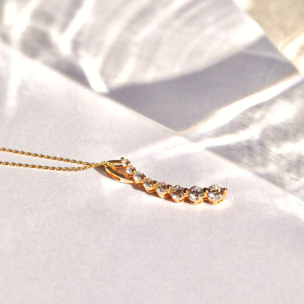 A 14K solid gold Cornicello pendant with a sleek, polished finish and delicate cubic zirconia accents, displayed on a plain and white background.