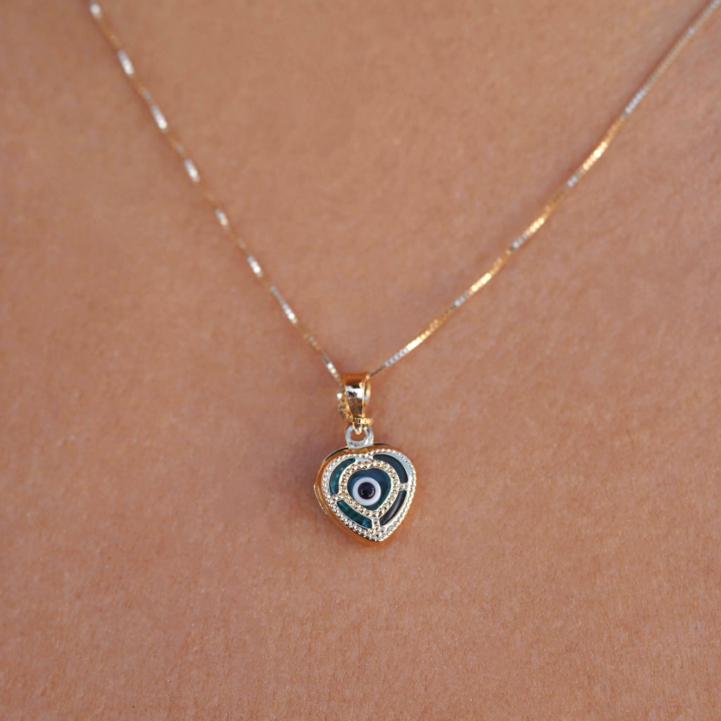 Model wearing a 14K yellow gold heart pendant with an evil eye center, showcasing elegant shine and dainty design against the skin.