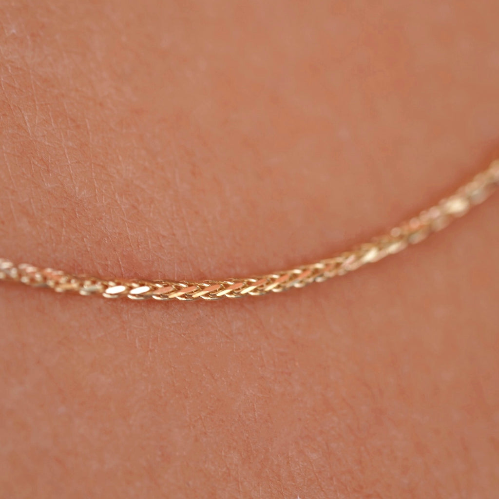 A model wearing a 14K yellow solid gold wheat chain necklace with 1.5mm flat open links, styled with a casual outfit to show the necklace’s versatility for both everyday and formal wear.