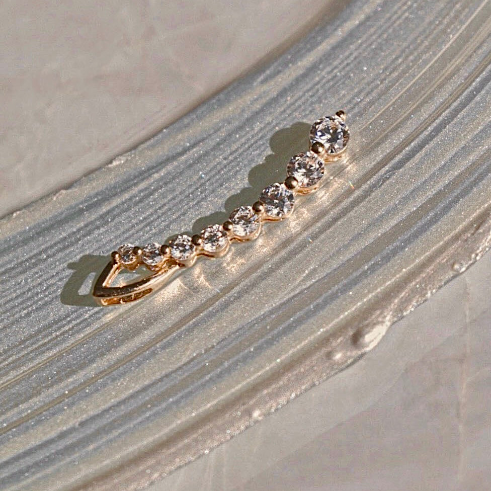 A 14K solid gold Cornicello pendant with a sleek, polished finish and delicate cubic zirconia accents, displayed on a silver backdrop.