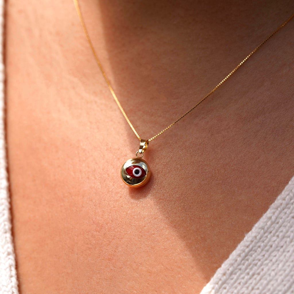 A model wearing a 14K yellow gold evil eye pendant with a red zirconia center on a fine gold chain, resting elegantly at her collarbone. The polished gold finish reflects light beautifully, highlighting the pendant’s delicate craftsmanship, symbolic protection, and subtle luxury from Tehrani Jewelry.