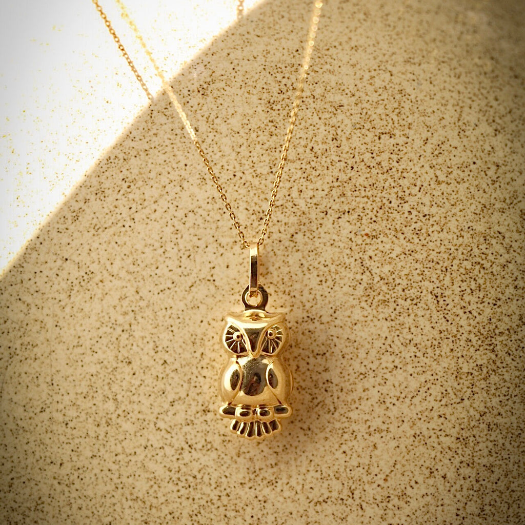 Dainty owl-shaped gold pendant styled on a neutral cloth background to showcase the warm gold tones and symbolic figure.