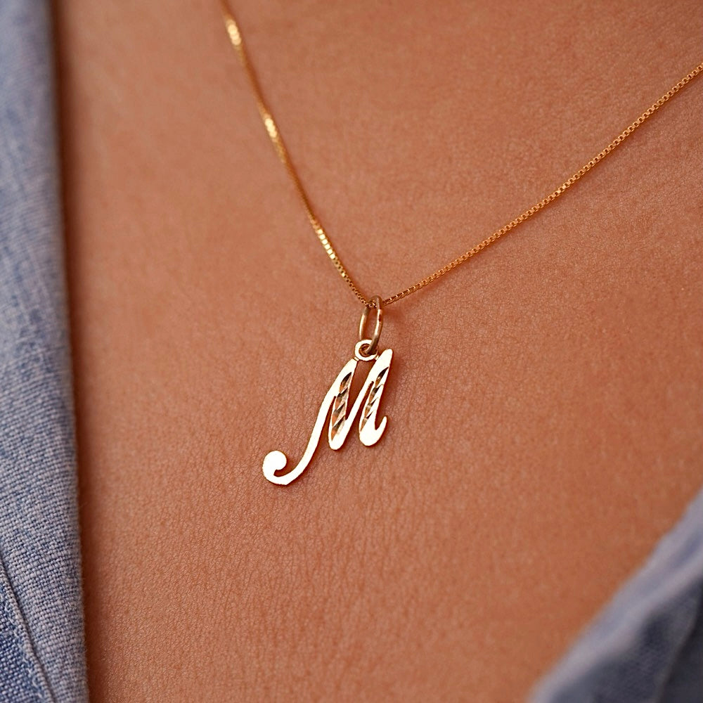 Model wearing a dainty gold initial M pendant, the charm sitting gracefully on her collarbone for a simple and personalized look.