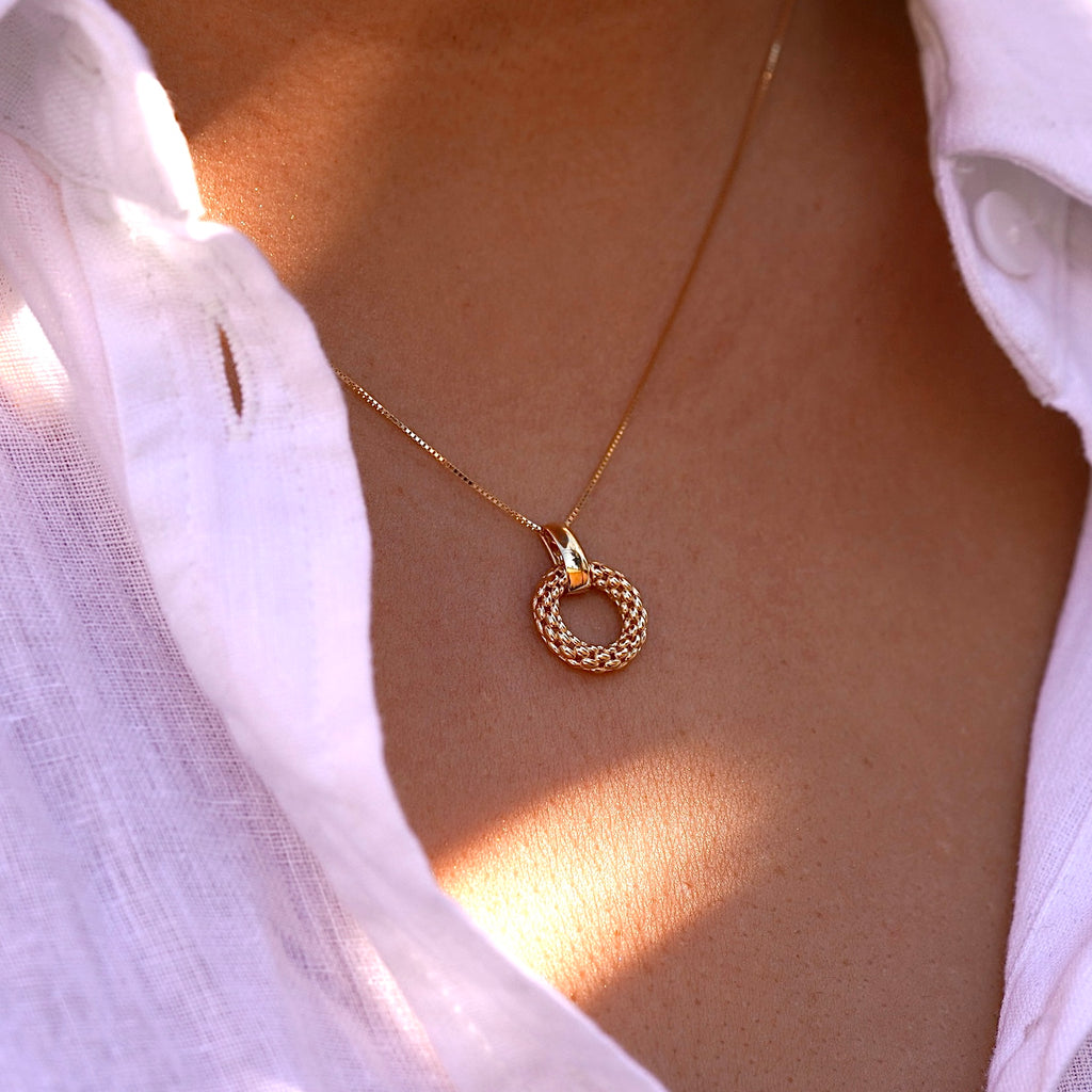 A woman wears the 14K gold mesh pendant on a dainty gold chain, the intricate filigree design resting gracefully against her collarbone. The lightweight and elegant pendant adds a timeless touch to her outfit.