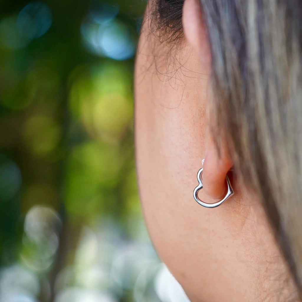 Model wearing dainty 14K white gold heart hoop earrings, with a radiant shine, highlighting the elegance and minimalist design of the earrings against a soft, natural background.