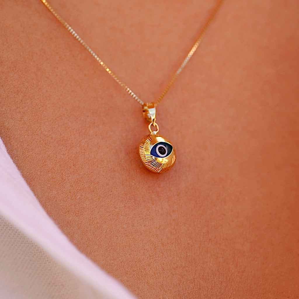 A model wears the 14K gold evil eye pendant with blue center on a fine chain, showcasing its dainty size and symbolic beauty as it rests just below the collarbone.