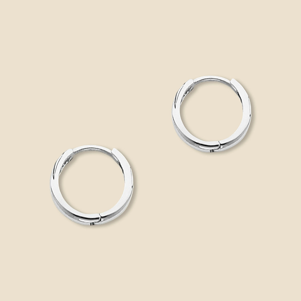A pair of small 14K white gold Huggies earrings shown against a plain backdrop, revealing the sleek curvature and 10mm diameter of each hoop.