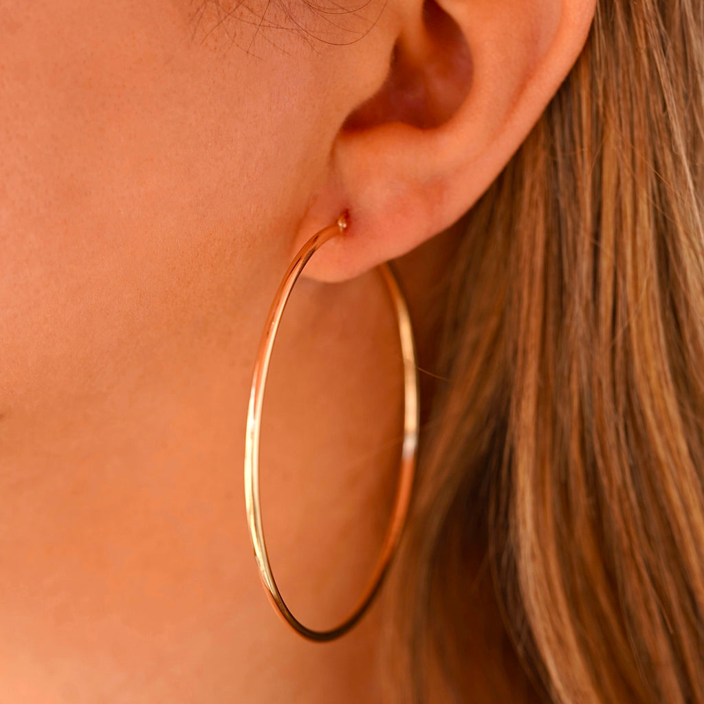 A woman wearing the 14K gold hoop earrings, highlighting their lightweight yet bold design, adding an elegant touch to her stylish outfit.