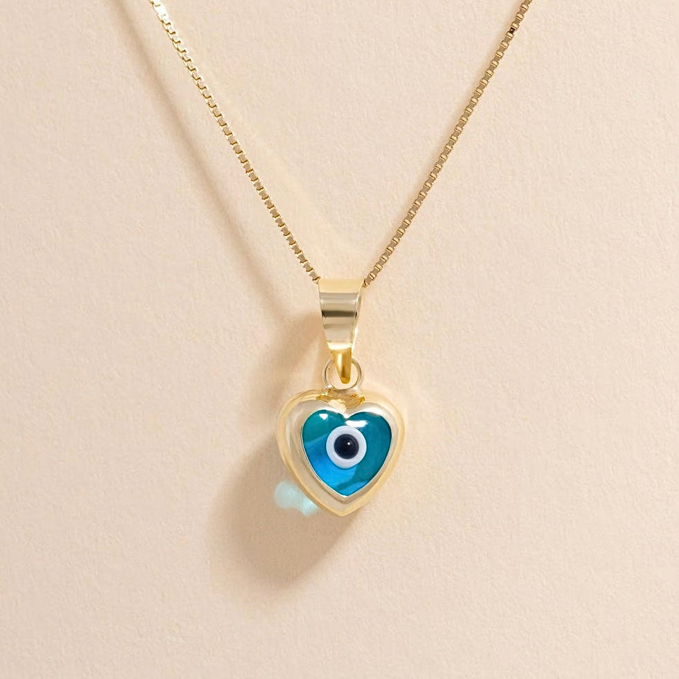 A close-up of the 14K yellow gold heart pendant with a vibrant blue evil eye center, resting on neutral and clean background, symbolizing classic protection and offering a minimalist yet bold pop of color.