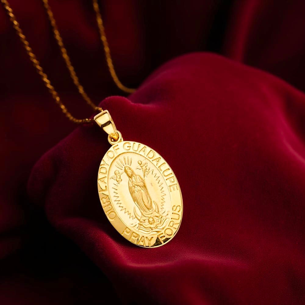 Close-up image of a 14K gold Guadalupe pendant laying on dark red velvet fabric, highlighting the detailed Virgin Mary engraving and lustrous yellow gold surface.