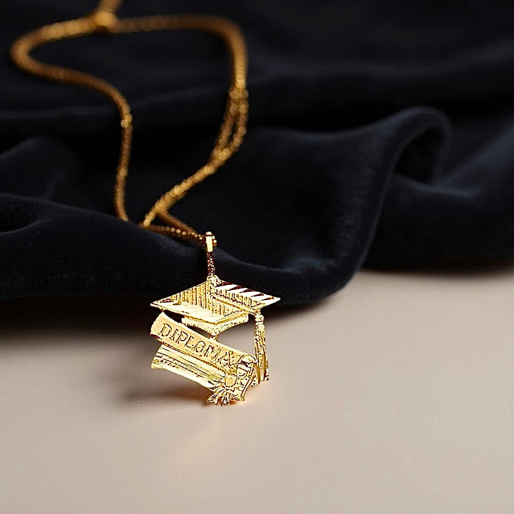 Elegant 14K Gold Graduation Cap Pendant resting on black fabric, highlighting its shine and fine detailing in a soft, natural setting.