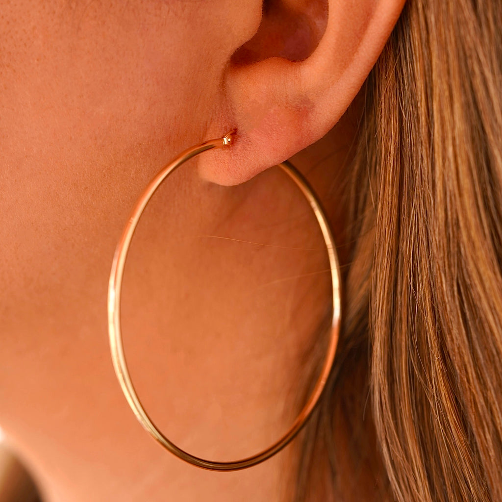 A woman wearing the 14K gold hoop earrings, highlighting their lightweight yet bold design, adding an elegant touch to her stylish outfit.