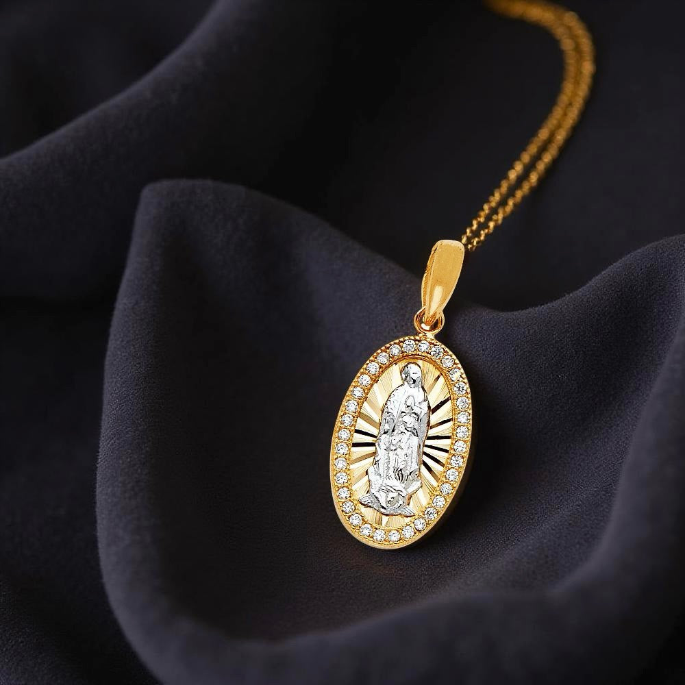 Close-up of 14K two-tone gold Our Lady of Guadalupe pendant resting on black fabric, highlighting the Virgin Mary detail surrounded by sparkling CZ accents.