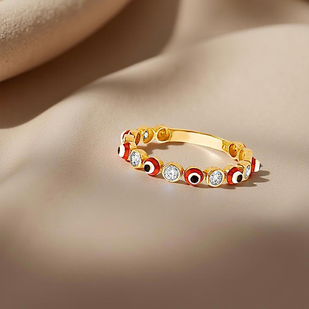 A dainty 14K yellow gold red evil eye ring placed on soft neutral cloth, capturing its glowing finish and vibrant red CZ center.