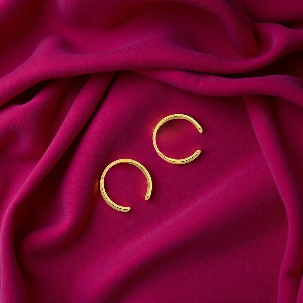 Minimalist gold ear cuff photographed on magenta fabric, highlighting its delicate curve and rich yellow hue.