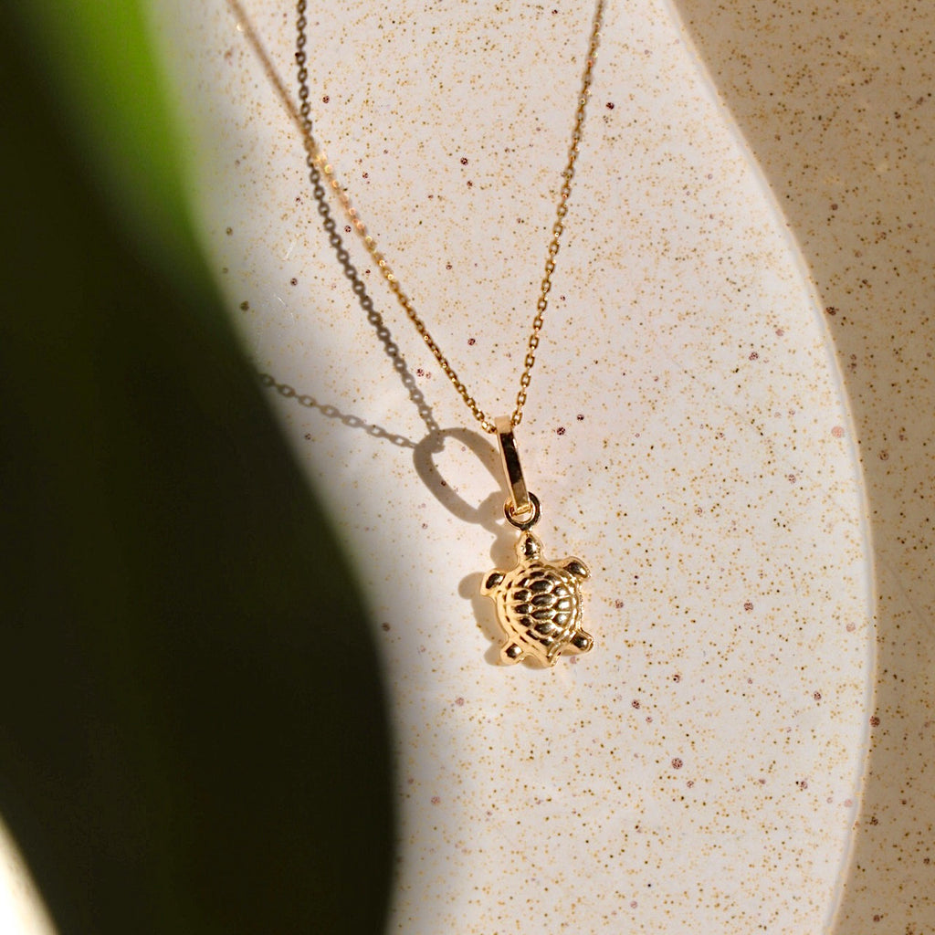 14K gold turtle pendant displayed on a white backdrop, highlighting its detailed craftsmanship and polished finish.