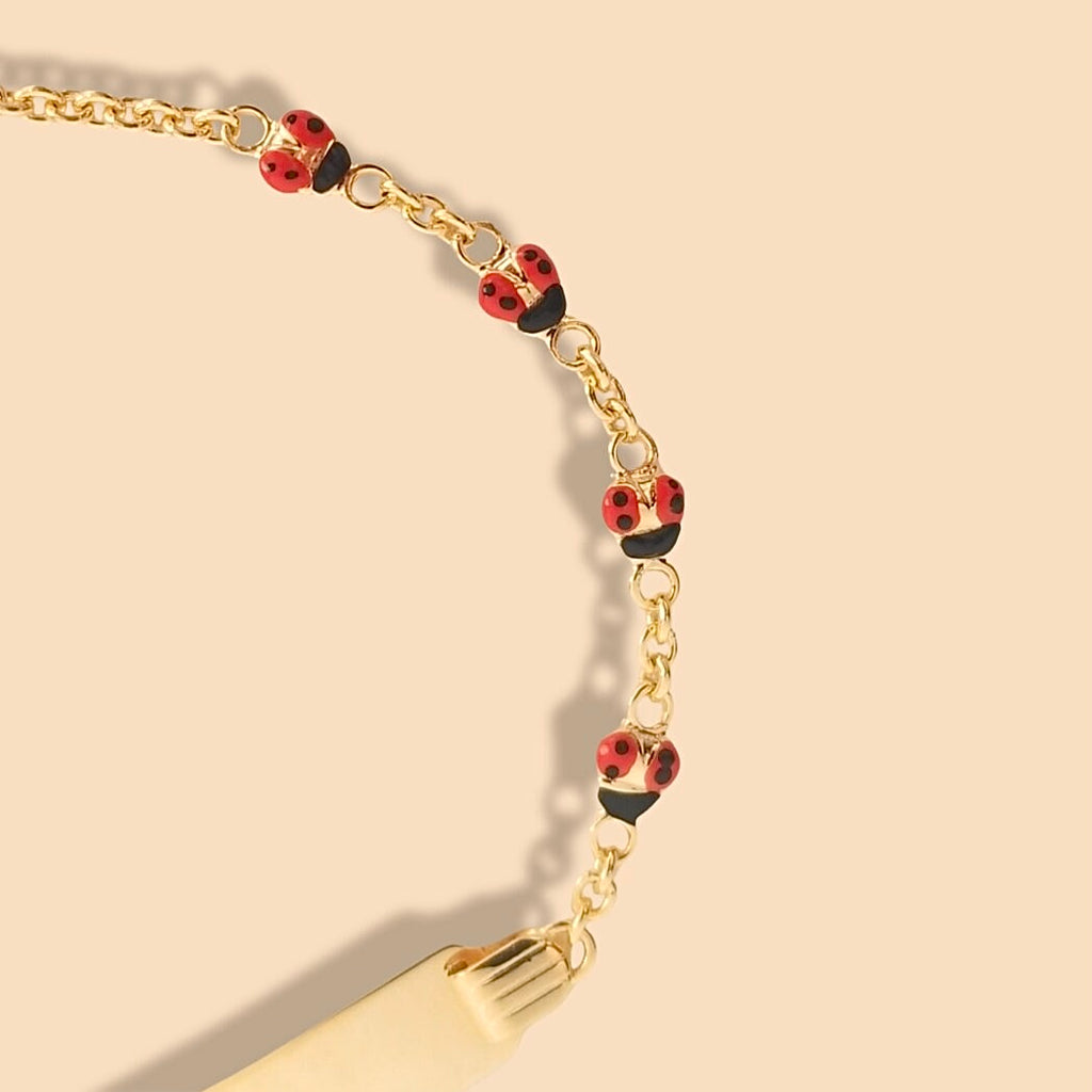 Close-up of 14k gold baby id bracelet with ladybug charm displayed on soft pink background, showing fine chain details and glossy finish.