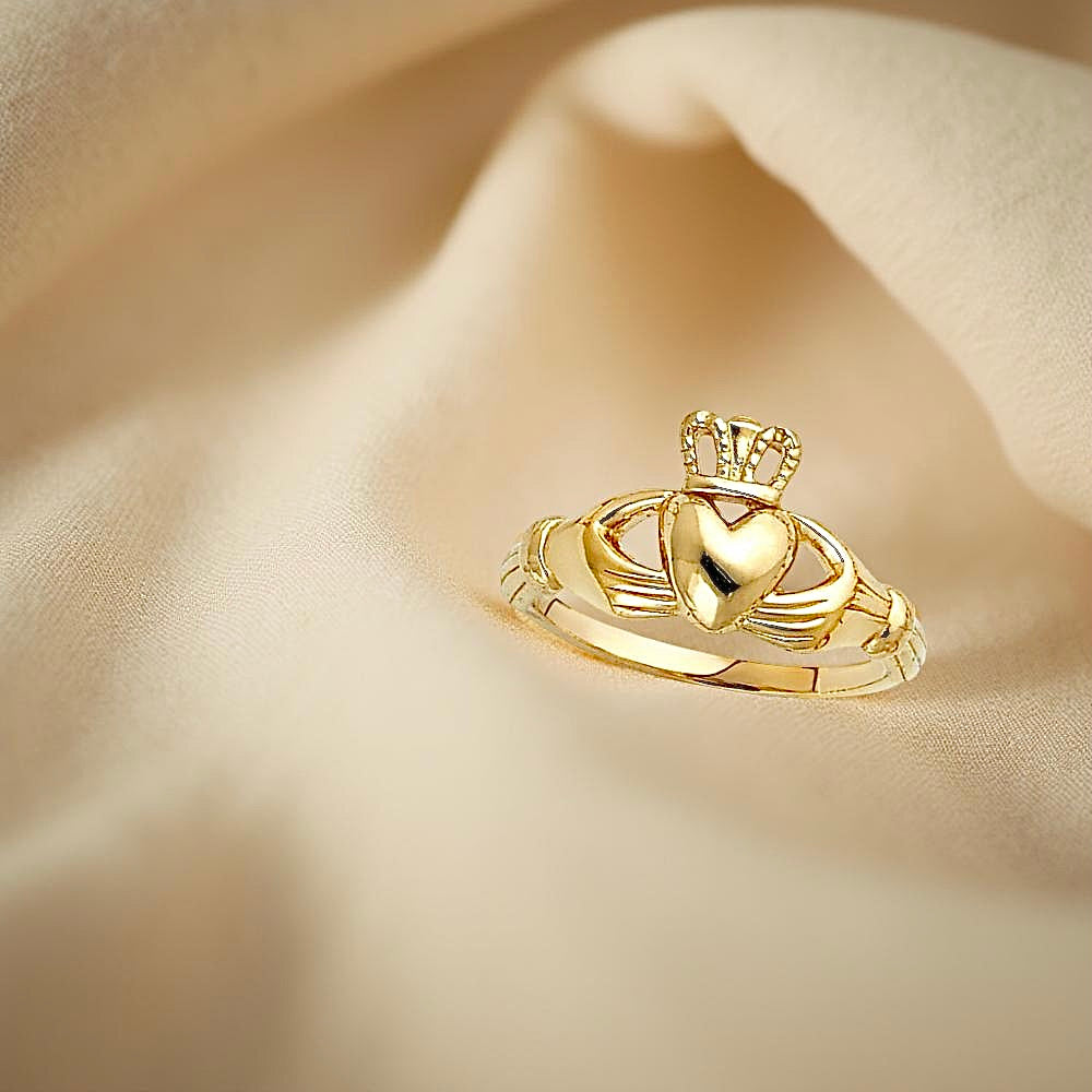 14K yellow gold Claddagh ring resting on soft off-white fabric, highlighting the heart, crown, and hands detail.