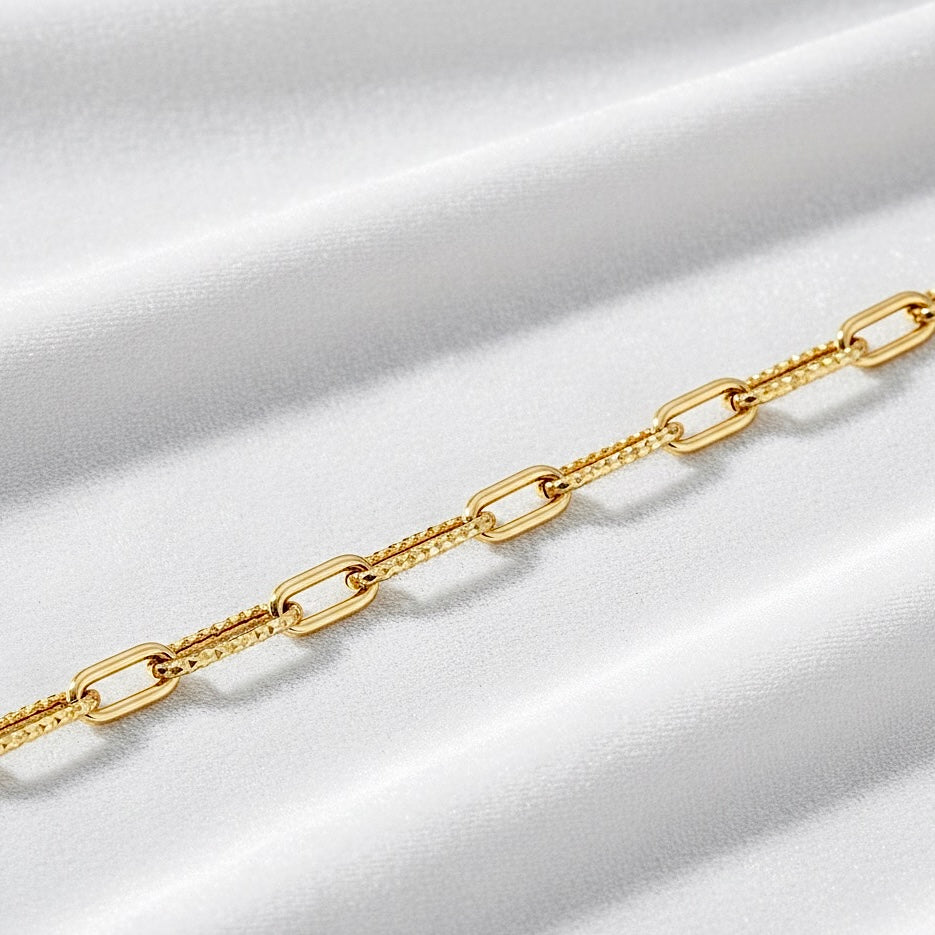 14K yellow gold paperclip 1+1 bracelet resting on soft white velvet cloth, showcasing its elegant design and warm gold tone against the textured fabric.