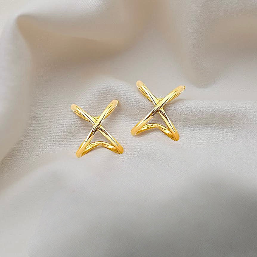 14K yellow gold X ear cuff resting on off-white fabric, highlighting its bold polished design.