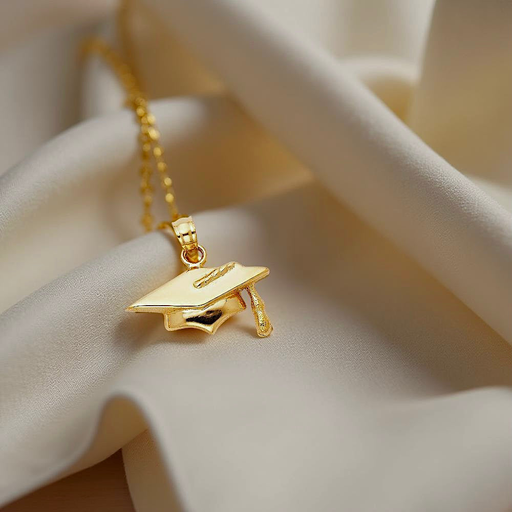 Elegant 14K Gold Graduation Cap Pendant placed on off-white fabric, highlighting its craftsmanship and rich golden hue in natural light.