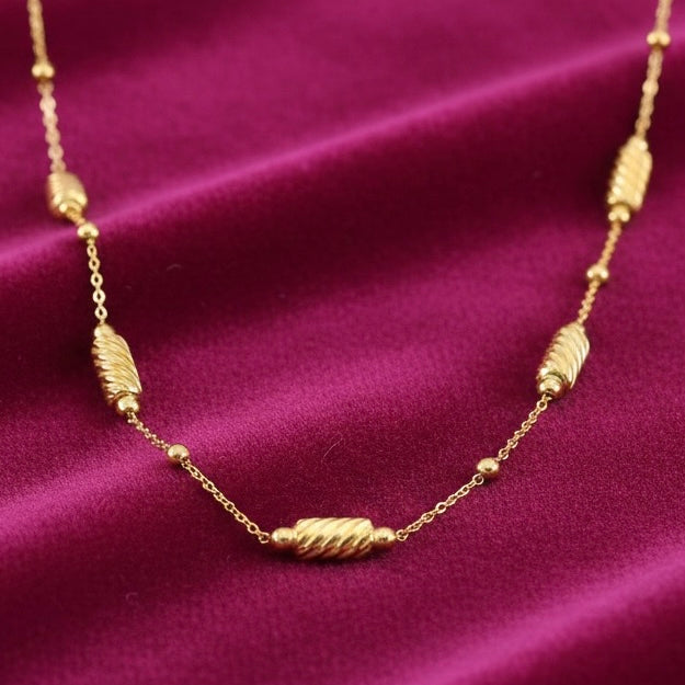 14K yellow gold long bead necklace laid on a rich magenta velvet, highlighting the sparkle of its diamond-cut beads against the soft textured fabric.