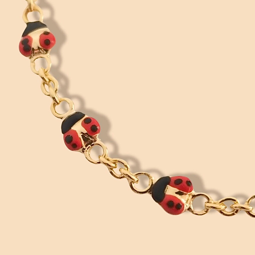 Close-up of 14k gold baby id bracelet with ladybug charm displayed on soft pink background, showing fine chain details and glossy finish.