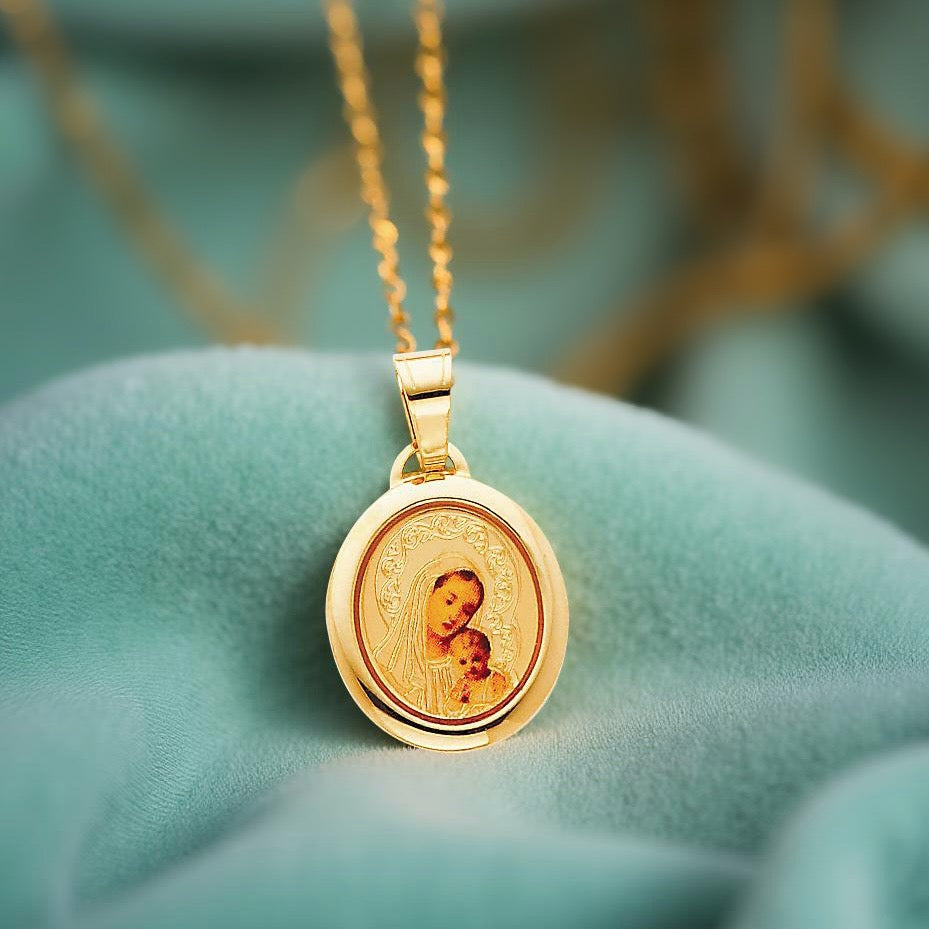 14K yellow gold Our Lady of Mt. Carmel pendant resting gently on a light blue fabric, showcasing the detailed Virgin Mary design in a radiant oval frame.