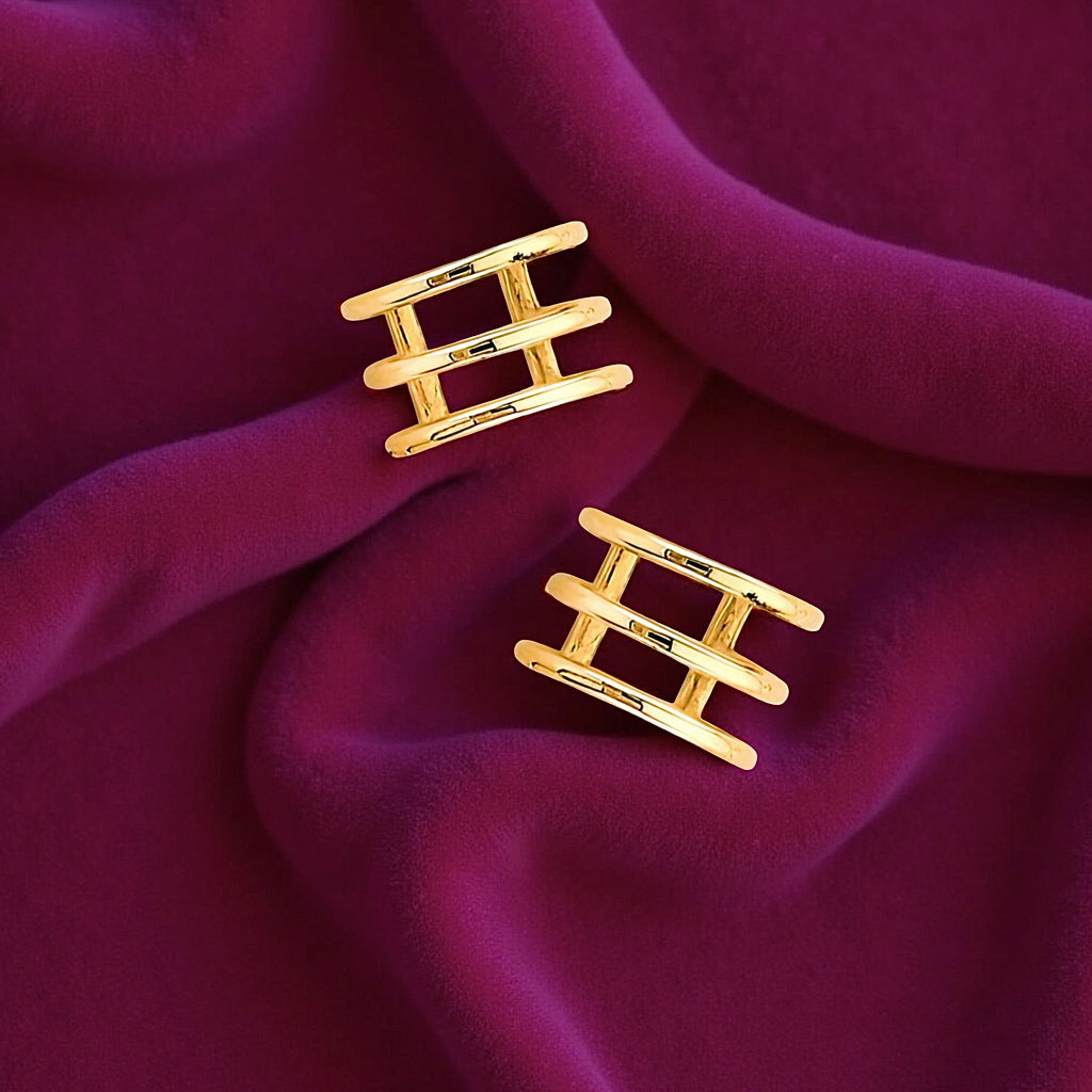 Dainty triple band ear cuff in 14K gold resting on a magenta velvet fabric, highlighting its smooth curves and luxury shine.