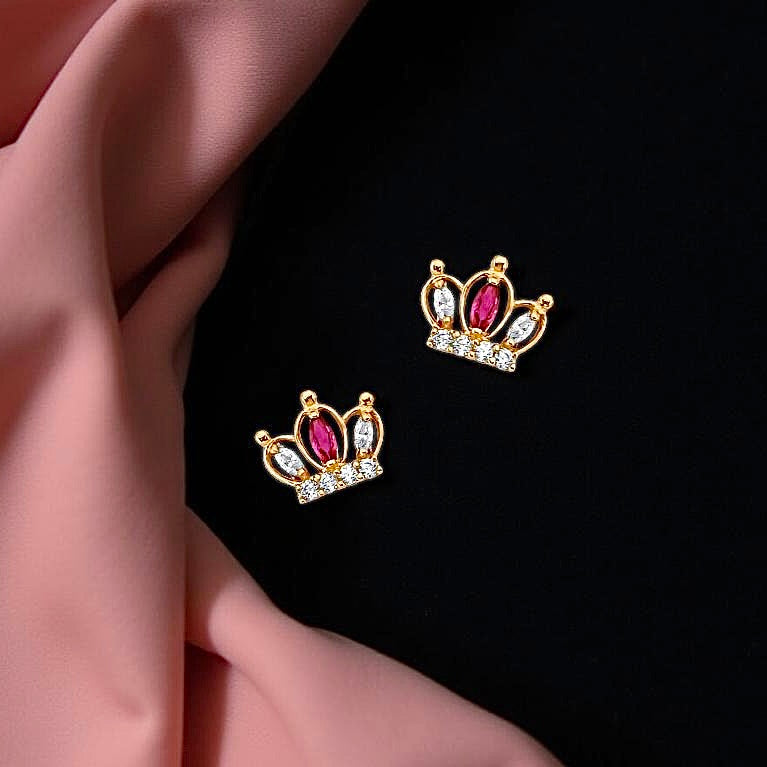 A pair of 14K gold crown-shaped CZ earrings resting on black and pink cloth, showcasing their sparkle and polished finish.