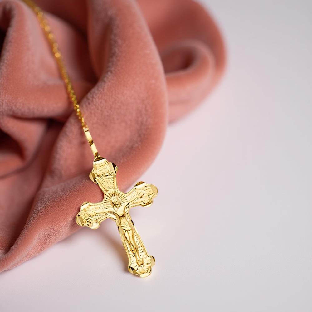 14K yellow gold crucifix pendant resting on dusty-rose velvet cloth, highlighting the fine detailing of the cross and figure of Christ.