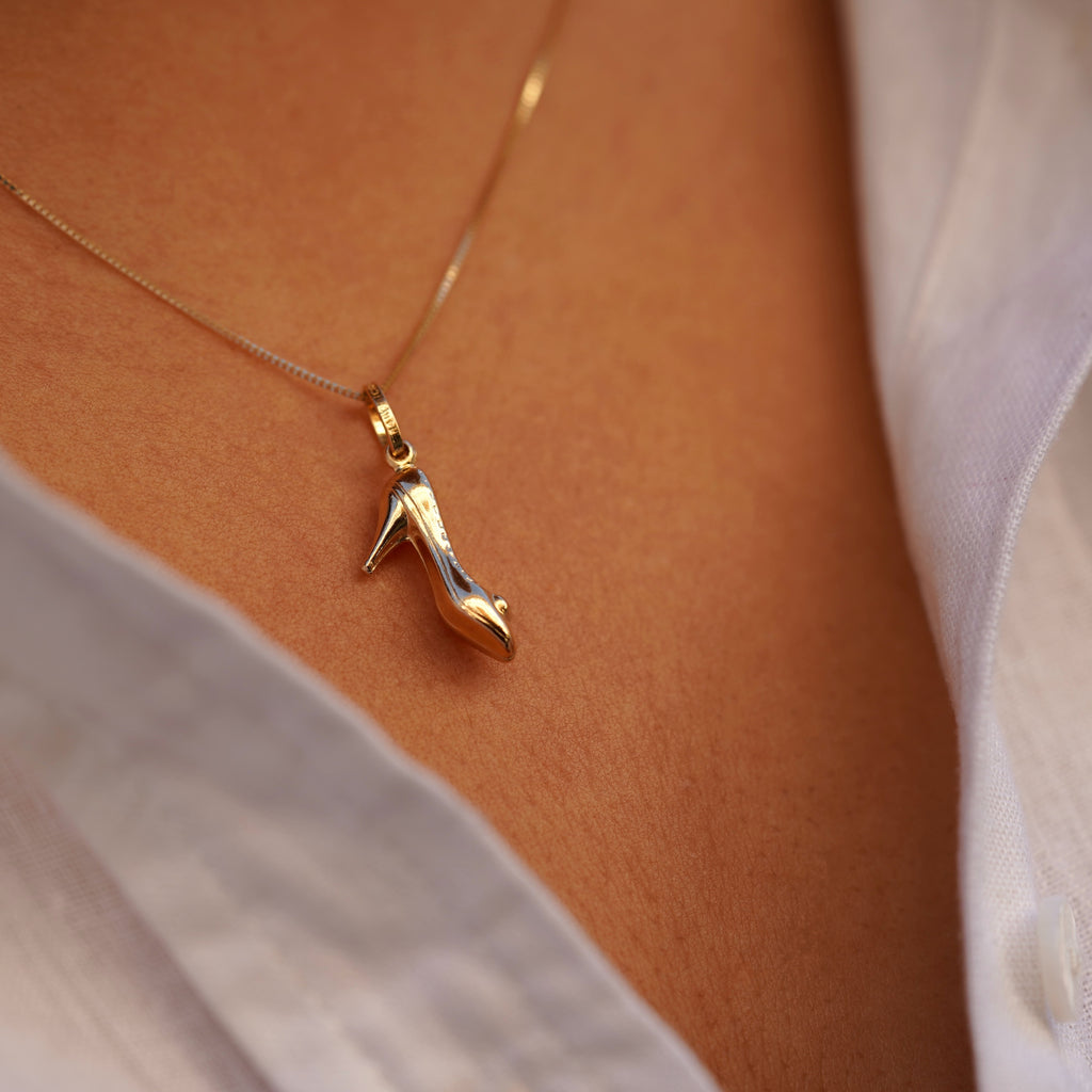 A model wearing the 14K solid gold high heel shoe charm pendant on a delicate gold chain around the neck. The charm rests just below the collarbone, adding a stylish and subtle touch to the model’s outfit. The lighting highlights the pendant’s rich yellow gold hue and refined craftsmanship, illustrating how this dainty charm enhances any fashion look with sophistication.