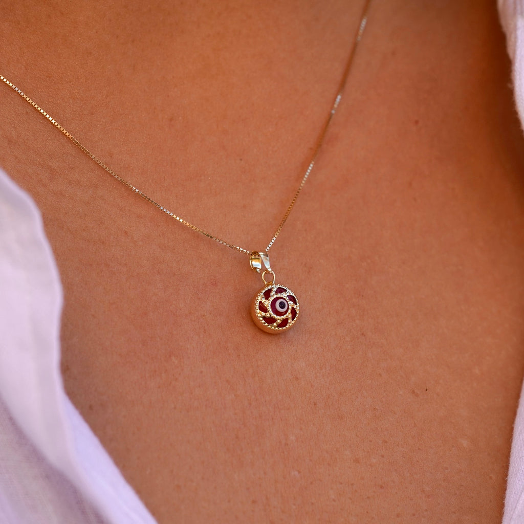 A model is wearing the 14K gold Evil Eye pendant with a red eye on a fine chain, allowing the charm to rest beautifully against the skin. The striking red eye adds a subtle yet meaningful touch, perfect for everyday wear.
