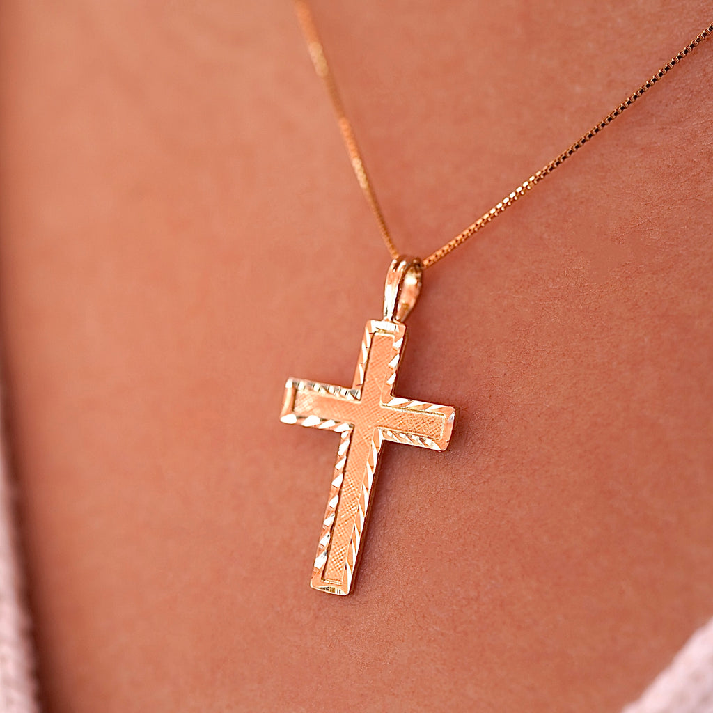 A model wearing the gold Latin cross pendant on a delicate chain, the charm sitting gracefully on her neckline with a soft glow.