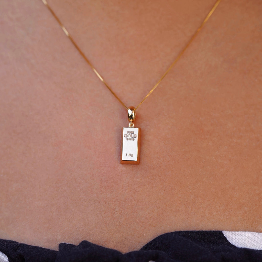 Close-up of a model wearing a 14K yellow gold bar pendant, the gleaming gold piece catching the light and offering a modern, refined jewelry statement.