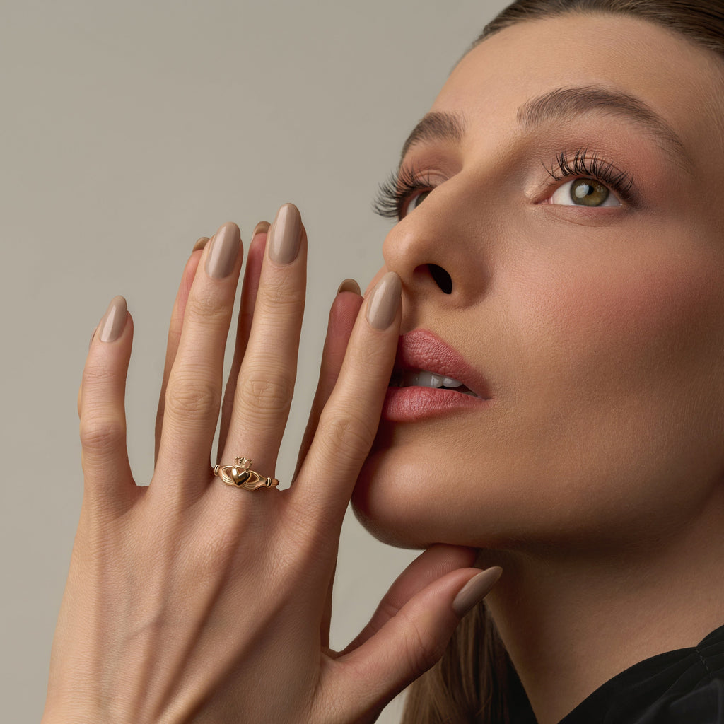 Model wearing a 14K solid yellow gold Claddagh ring on her hand, showcasing the traditional heart, crown, and hands design against a plain background.