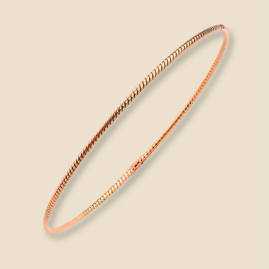A dainty 14K rose gold braided bangle bracelet with a delicate 1.5mm rope design, placed against a plain background. The warm golden tone and intricate twist pattern reflect light softly, highlighting the elegant craftsmanship.
