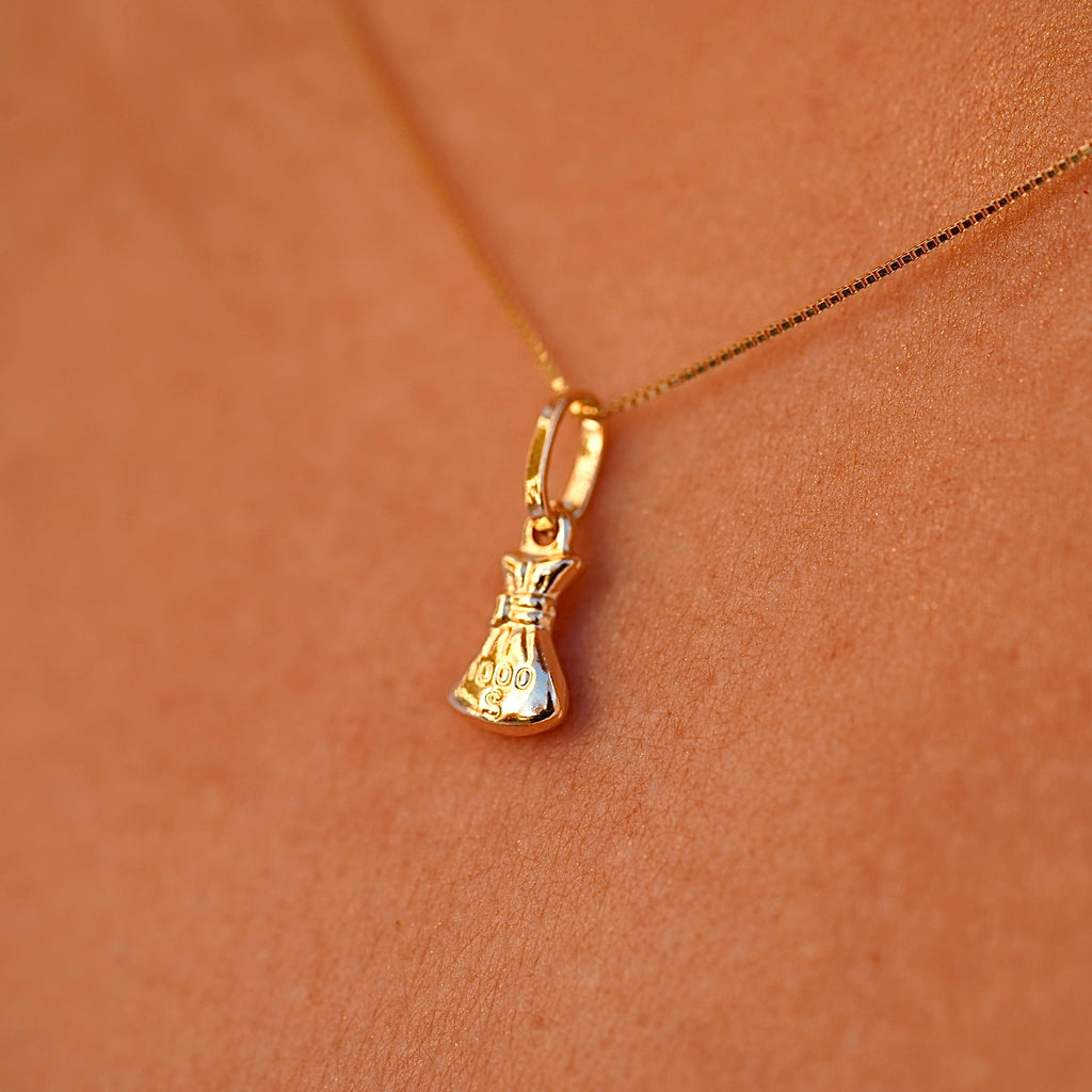 A model wearing a 14K gold money bag pendant on a delicate chain, showcasing its elegant and dainty size as it complements her outfit.