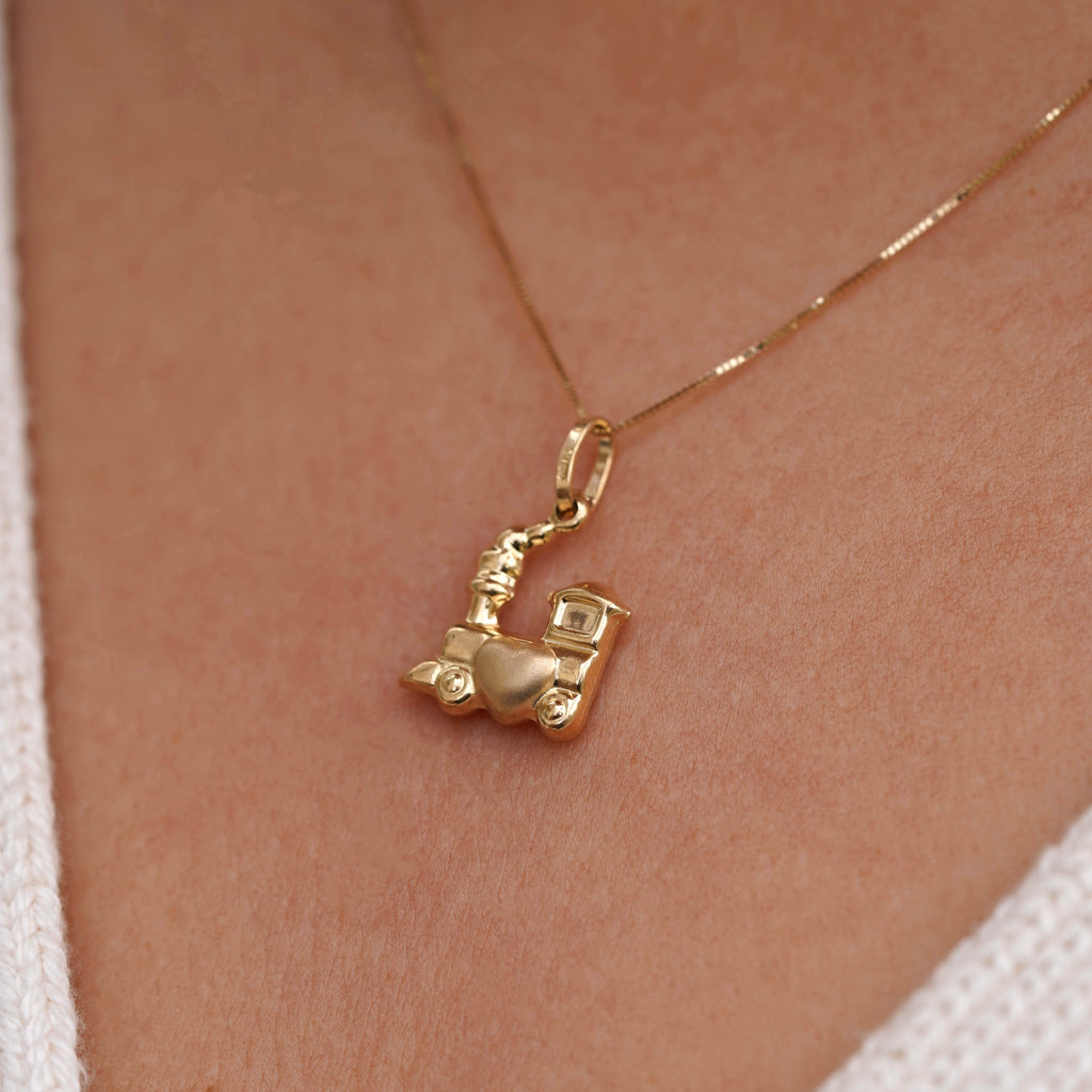 Close-up of a model wearing a 14K yellow gold Train of Love pendant on a delicate gold chain, the polished train-shaped charm resting elegantly at her collarbone against a simple blouse.