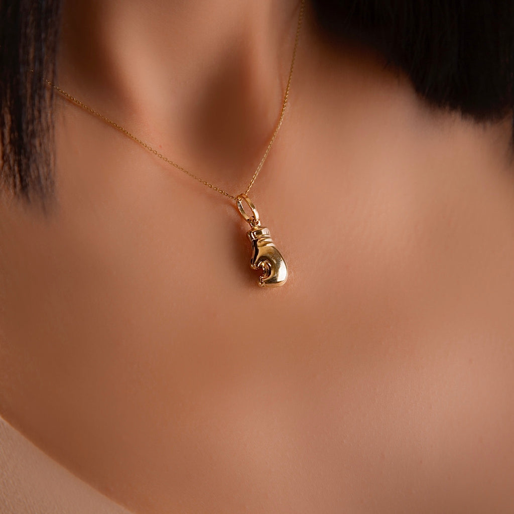 14K Gold Boxing Glove Pendant worn by a model, resting stylishly on the neckline, symbolizing strength and determination.
