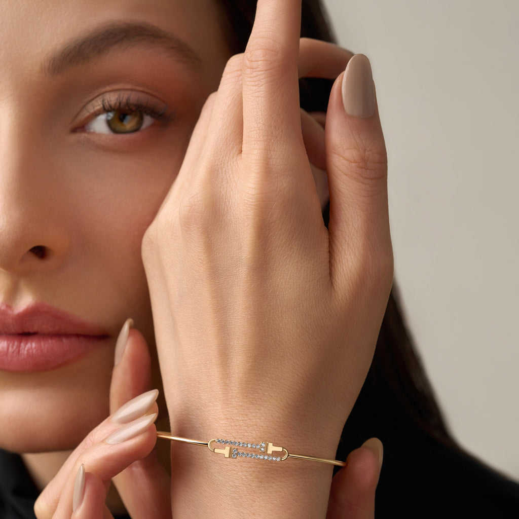 A model elegantly wearing a 14K yellow gold flexible bangle adorned with brilliant cubic zirconia stones. The bracelet glimmers softly under the light, highlighting its sleek, minimalist design and lightweight flexibility. The model’s wrist showcases how the bangle curves naturally for a comfortable, refined fit, perfect for everyday sophistication or special occasions. The yellow gold finish radiates warmth and luxury, complementing any modern, elegant style.