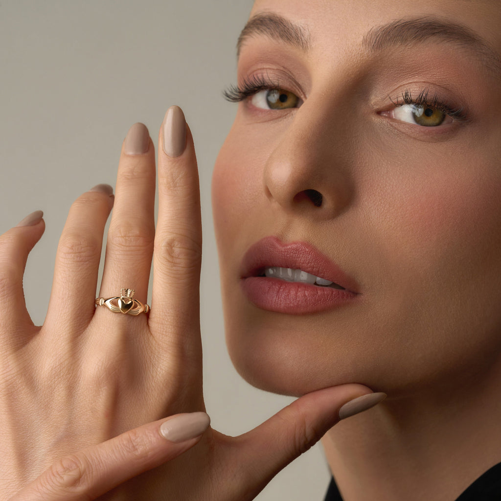 Model wearing a 14K solid yellow gold Claddagh ring on her hand, showcasing the traditional heart, crown, and hands design against a plain background.