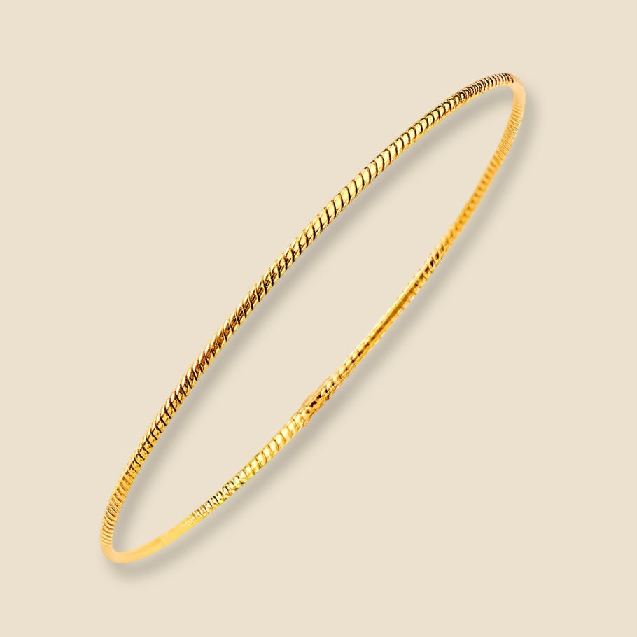 A dainty 14K yellow gold braided bangle bracelet with a delicate 1.5mm rope design, placed against a plain background. The warm golden tone and intricate twist pattern reflect light softly, highlighting the elegant craftsmanship.