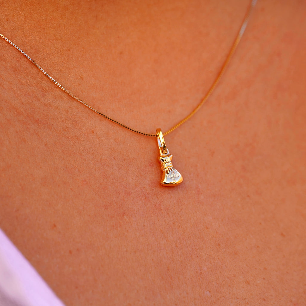 A model wearing a 14K gold money bag pendant on a delicate chain, showcasing its elegant and dainty size as it complements her outfit.