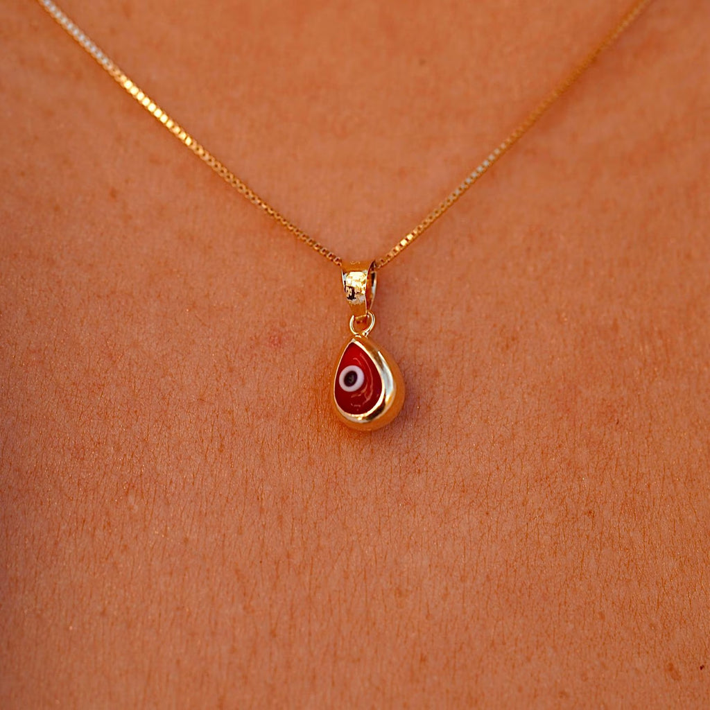A model wears the 14K Gold Tiny Tear Evil Eye Charm with the bold red eye, making a striking and meaningful statement.