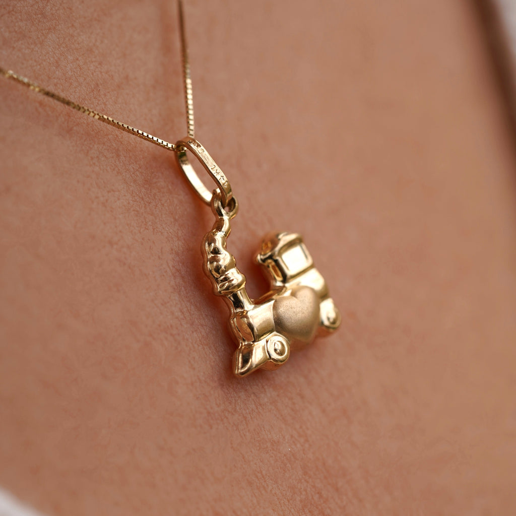 Close-up of a model wearing a 14K yellow gold Train of Love pendant on a delicate gold chain, the polished train-shaped charm resting elegantly at her collarbone against a simple blouse.