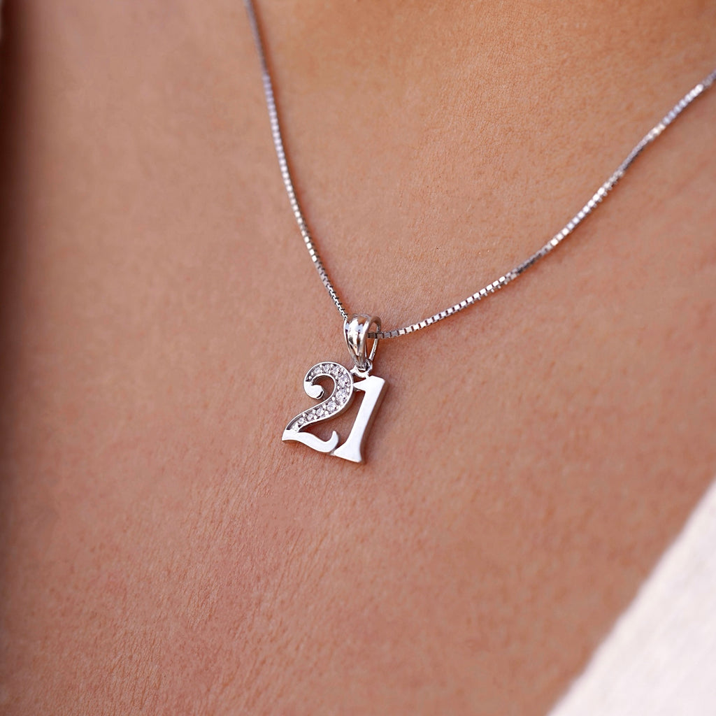 A model wears the 14K white gold "21 Years" charm pendant on a matching white gold chain, with cubic zirconia sparkling subtly under natural light—capturing the elegance and significance of a milestone birthday.