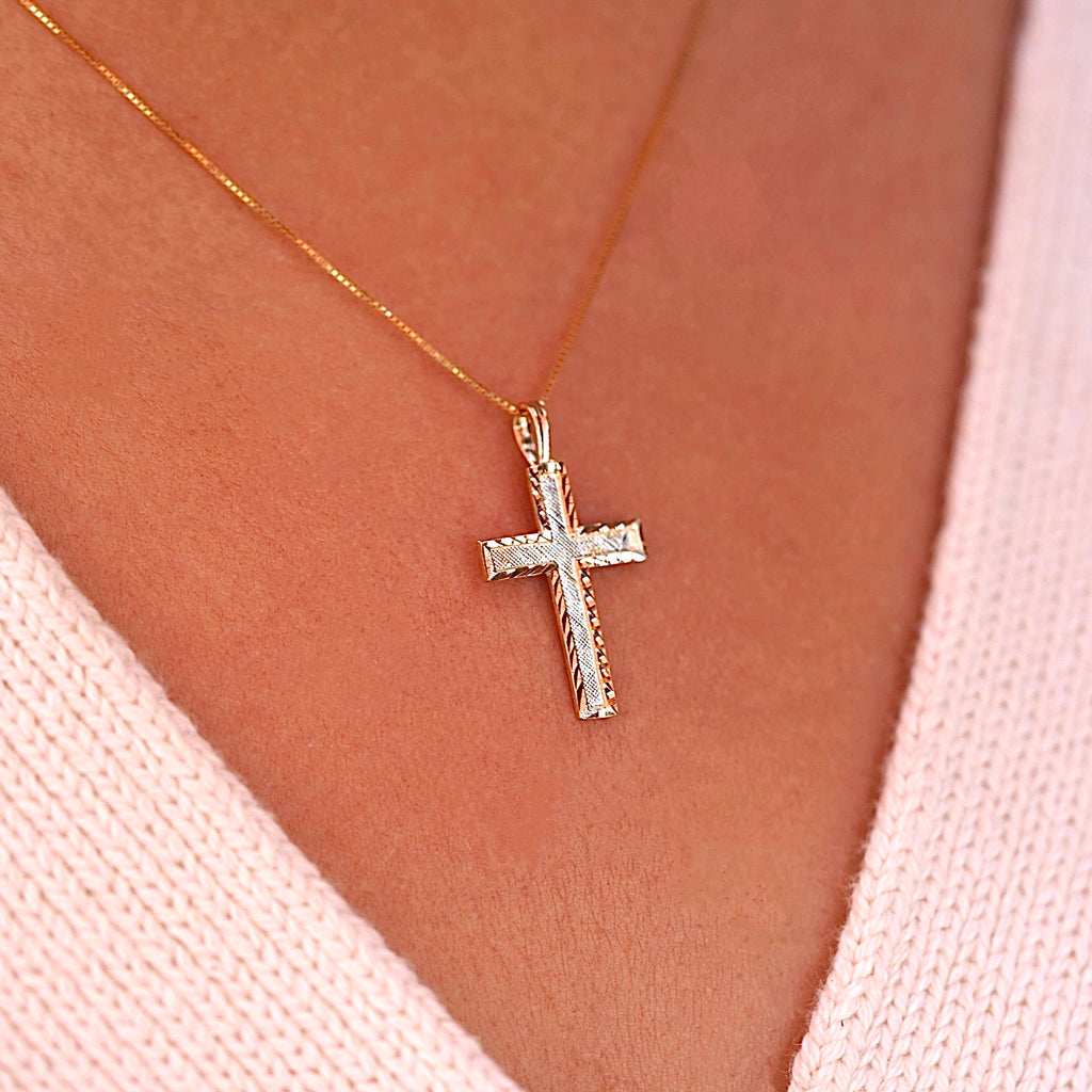A model wearing the gold Latin cross pendant on a delicate chain, the charm sitting gracefully on her neckline with a soft glow.