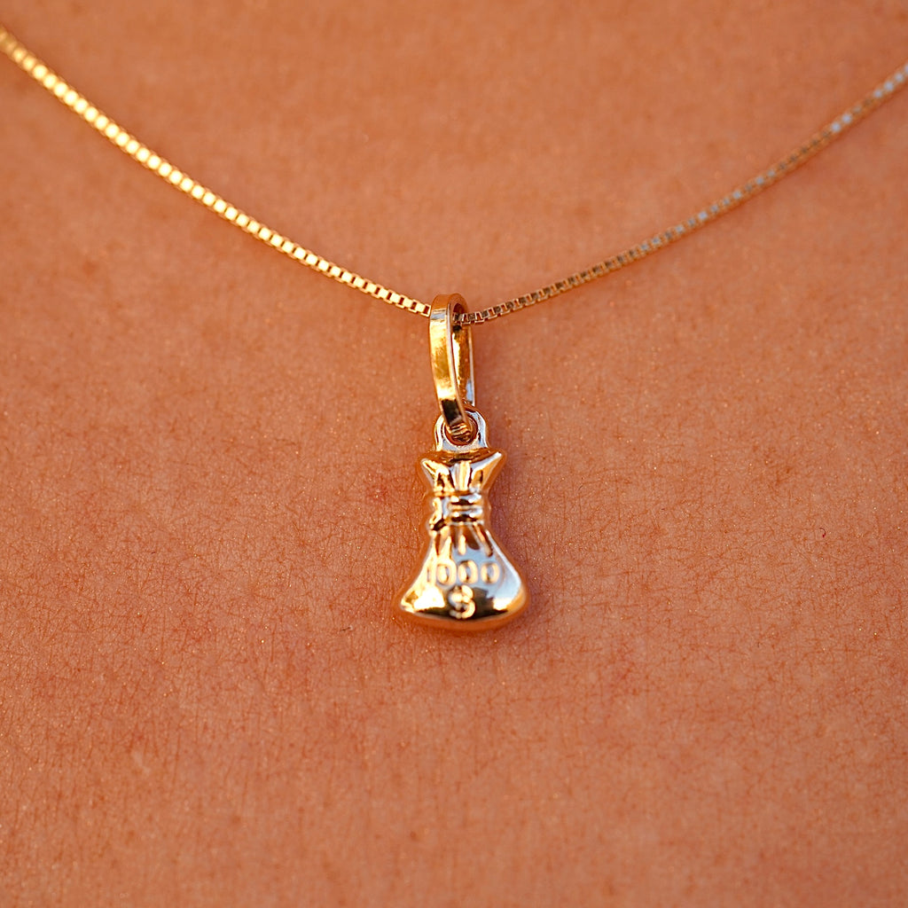 A model wearing a 14K gold money bag pendant on a delicate chain, showcasing its elegant and dainty size as it complements her outfit.